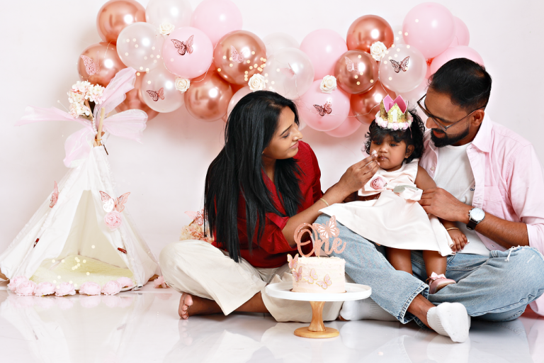 Parents celebrating their baby girl first birthday with a cake and pink balloon setup, family cake smash photoshoot in Doha
