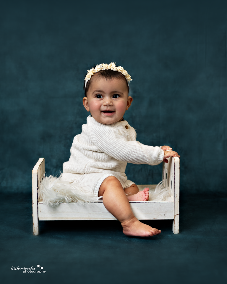 Happy baby sitting on a small white bed on a teal backdrop