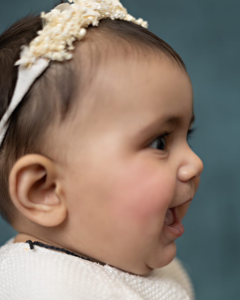 Close-up profile of a laughing baby girl with a flower headband