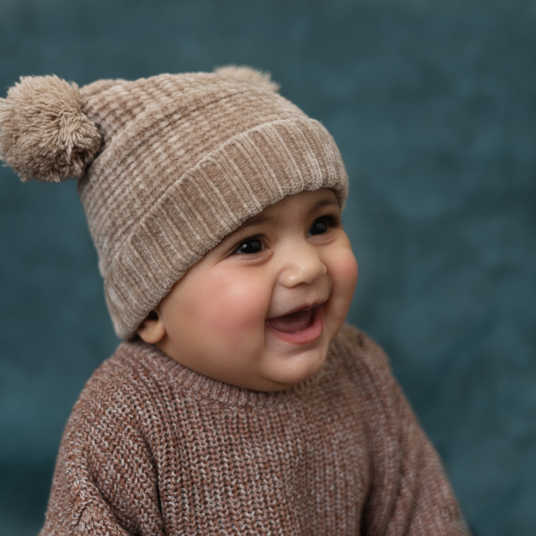 Laughing baby in a knitted pom-pom hat and brown sweater, 6 month baby photoshoot in Doha