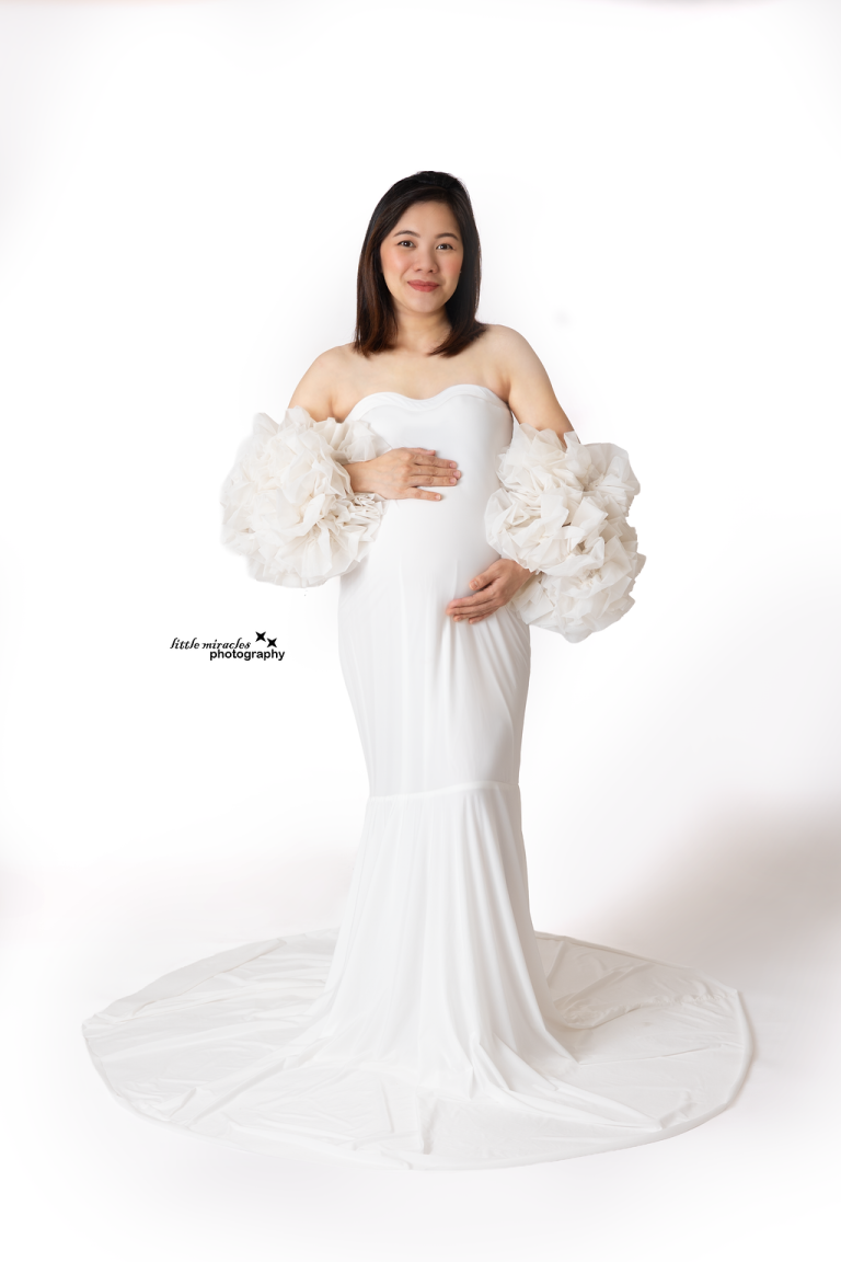 Pregnant woman in a white off-shoulder gown with ruffled sleeves