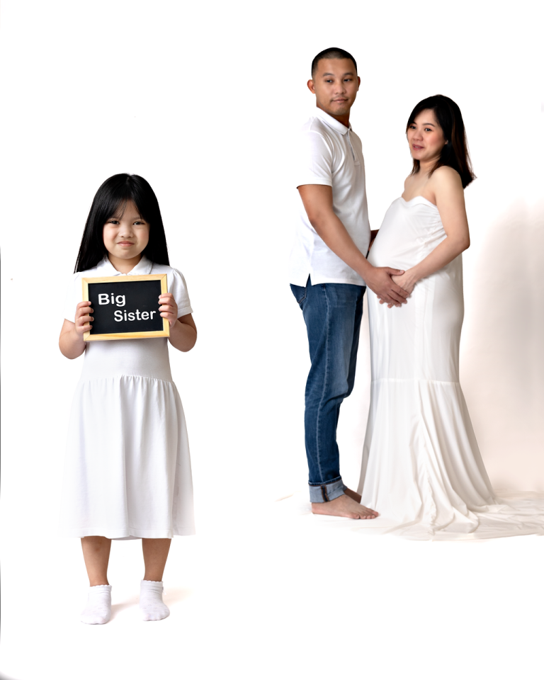 Expecting parents with their daughter holding a Big Sister sign during a family maternity photoshoot in Doha