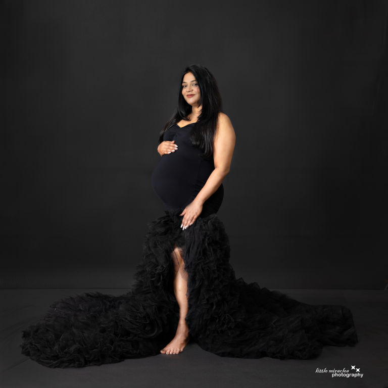 Pregnant woman in a black tulle maternity gown with a long train on a dark backdrop, maternity photoshoot in Doha