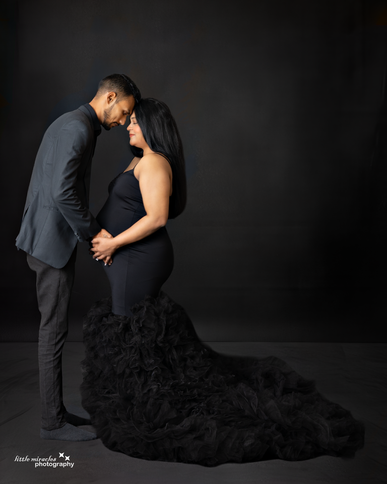 Expecting couple touching foreheads, woman in a black tulle gown