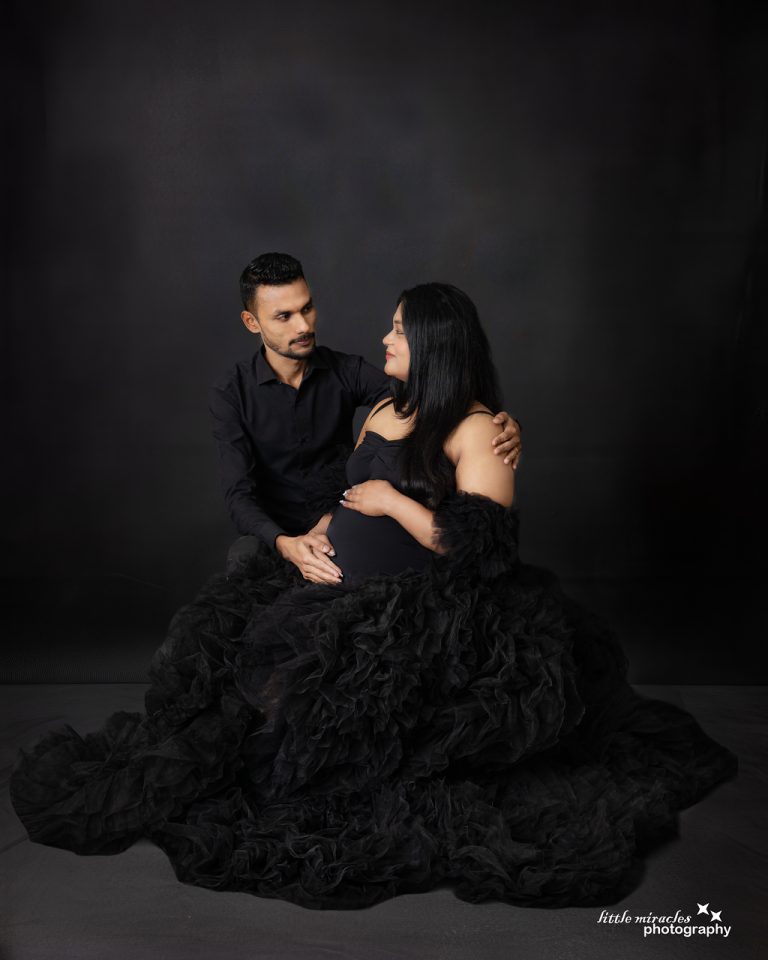 Expecting couple in matching black outfits with a black tulle gown on a dark backdrop, maternity photoshoot in Qatar