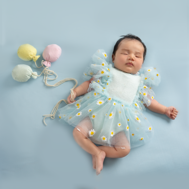 Sleeping newborn girl in a blue tulle dress with daisies and pastel balloons