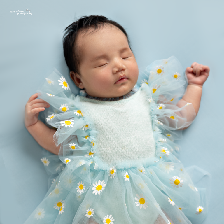 Close-up of a sleeping newborn girl in a blue ruffled dress with daisies