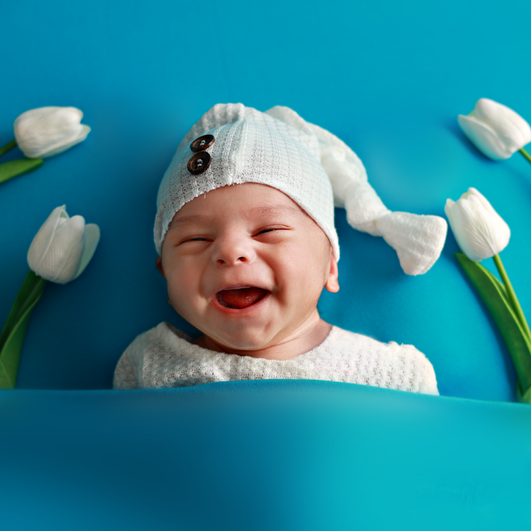 Smiling baby in a knitted hat with white tulips on a blue backdrop