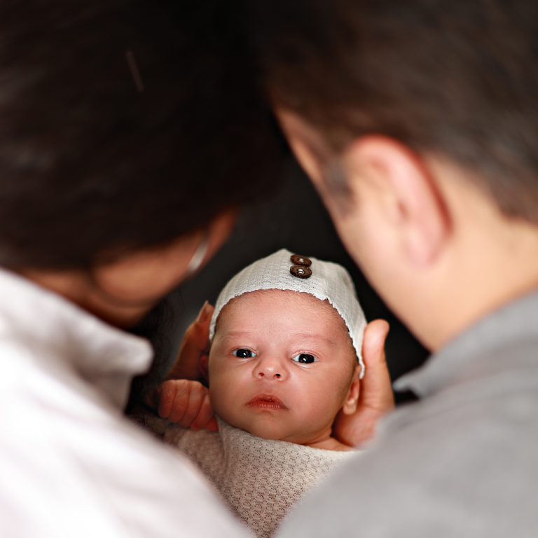 Newborn baby in a knitted hat looking up while held by his parents
