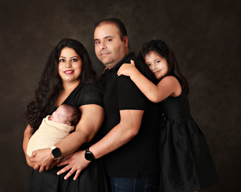 Parents with their newborn and daughter in black outfits on a dark backdrop, family portrait in Doha