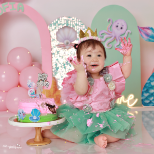 One-year-old girl in a crown playing with a pink mermaid cake, cake smash photoshoot in Doha