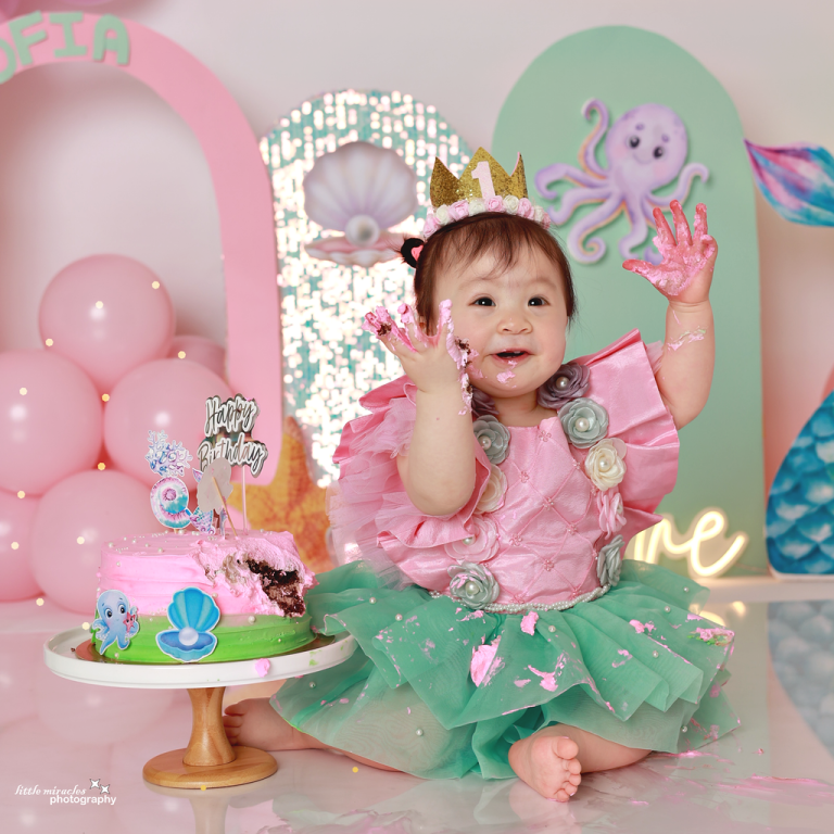One-year-old girl in a crown playing with a pink mermaid cake, cake smash photoshoot in Doha