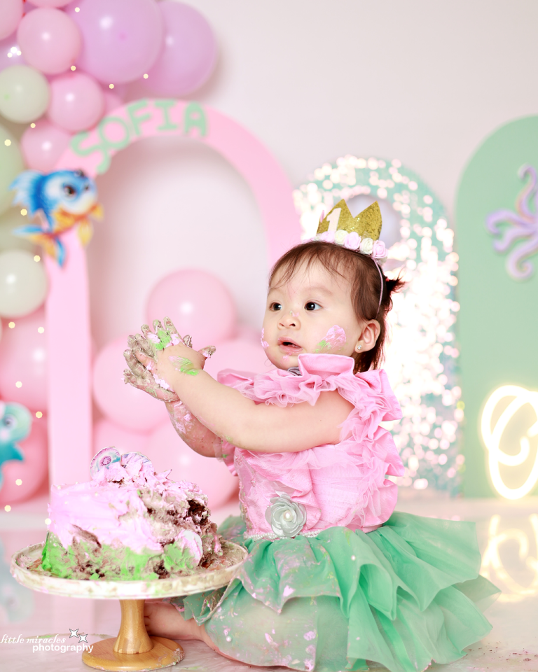 Baby girl exploring her mermaid cake with icing on her hands