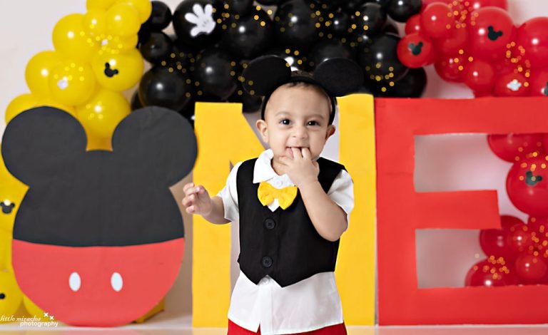 One-year-old boy in a waistcoat and bow tie at a Mickey Mouse "ONE" balloon setup