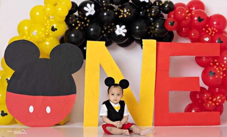 One-year-old boy in a waistcoat and bow tie with a Mickey Mouse ONE balloon setup, first birthday photoshoot in Doha