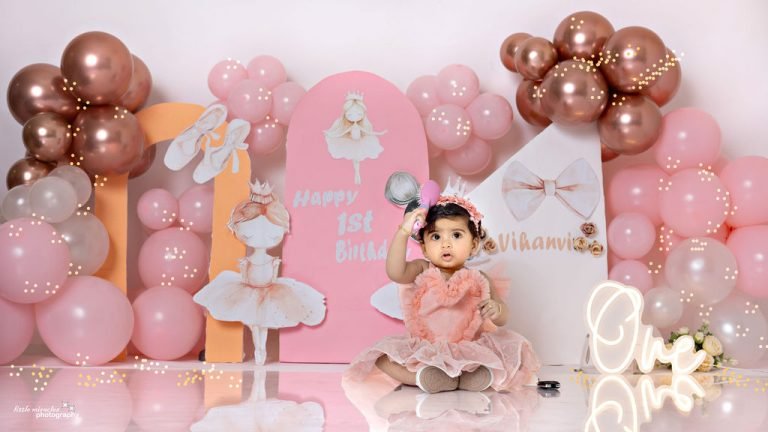 Baby girl at a pink and rose-gold first birthday setup with balloons