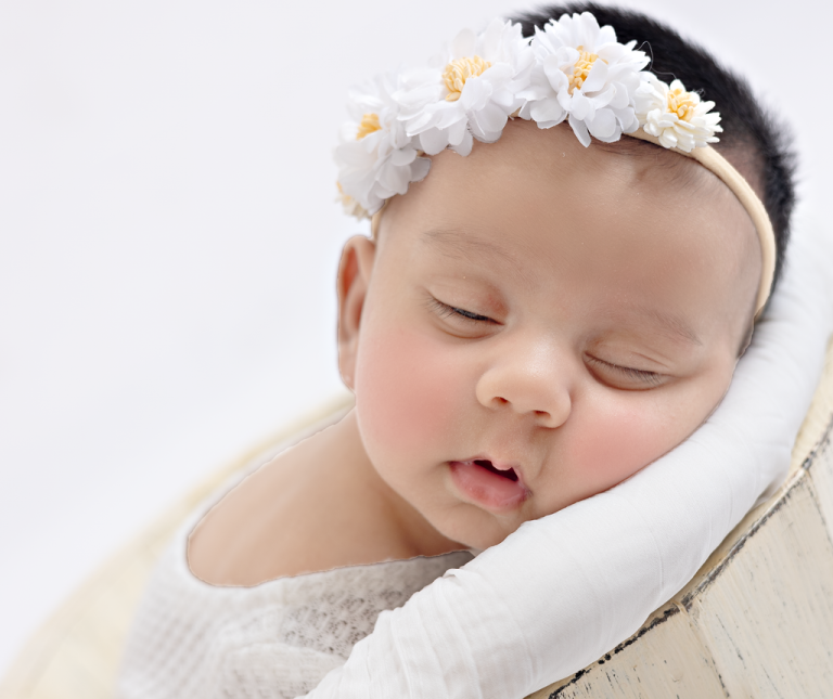 Close-up of a sleeping newborn girl wearing a white daisy headband