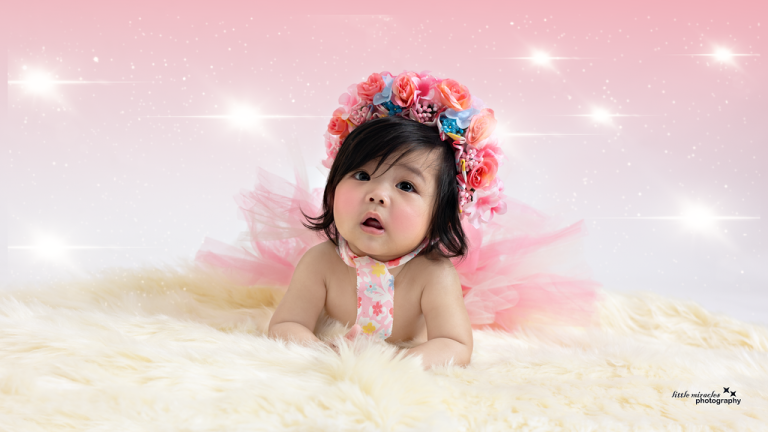 Baby girl in a flower crown and pink tutu lying on a fur rug with sparkles