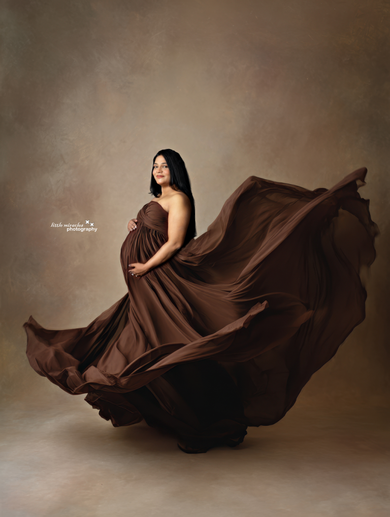 Pregnant woman in a flowing brown gown with the fabric in motion, maternity photography in Doha