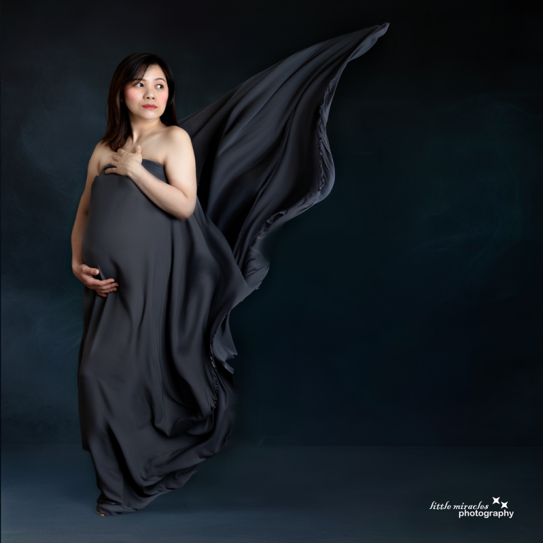 Mum-to-be in a dark flowing maternity gown with fabric in motion, elegant maternity photography in Doha