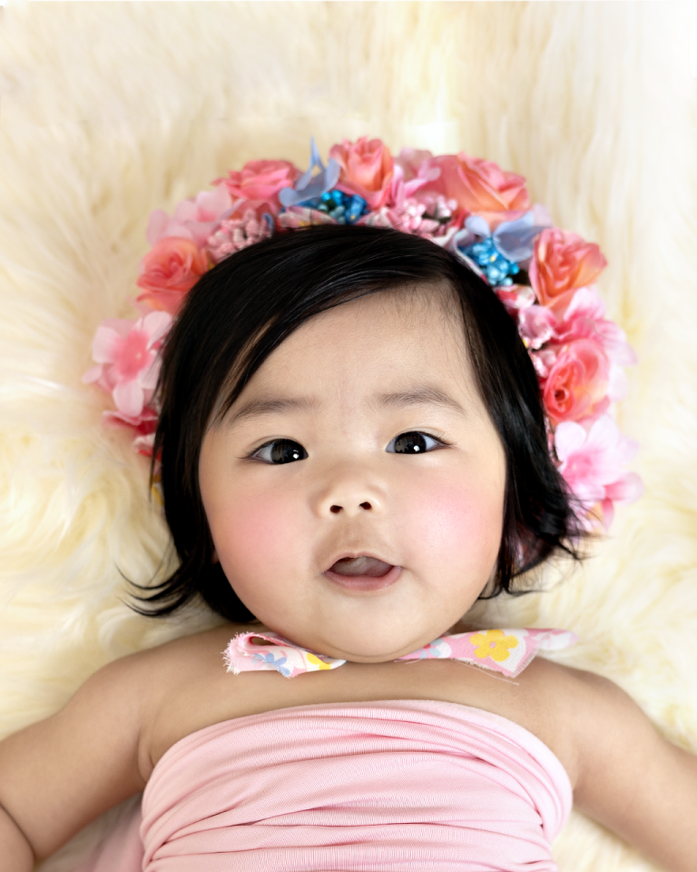 Close-up of a baby girl in a colourful flower crown lying on cream fur