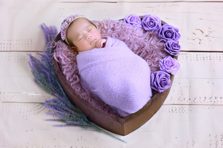 Sleeping newborn wrapped in lavender in a heart-shaped bowl with purple roses