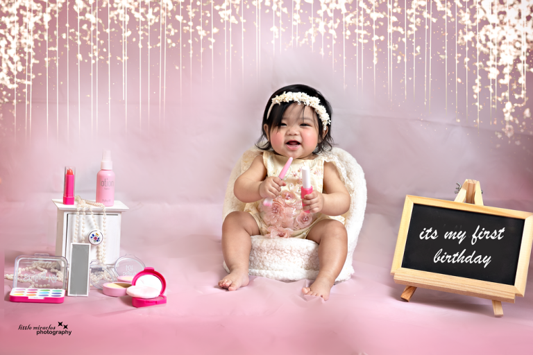 Baby girl at a pink "it's my first birthday" setup with a chalkboard sign