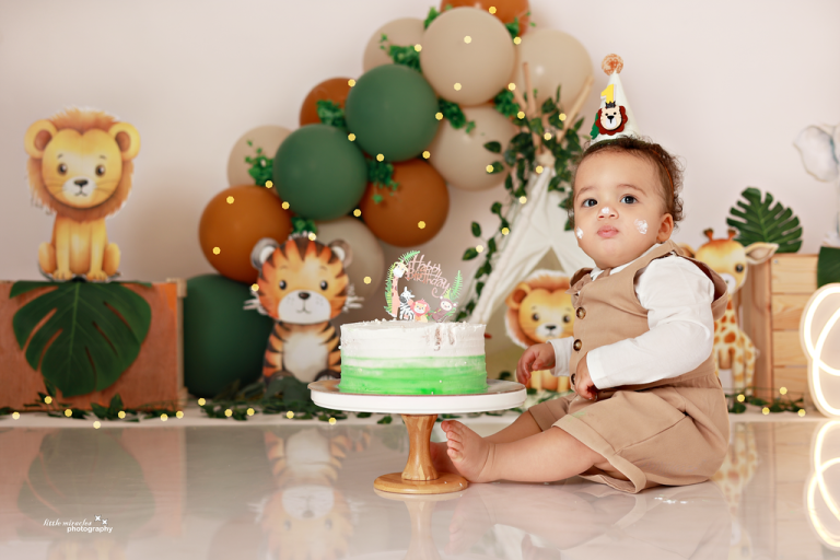 Baby sitting beside a green cake on a stand with a jungle safari animal theme, cake smash photography in Doha