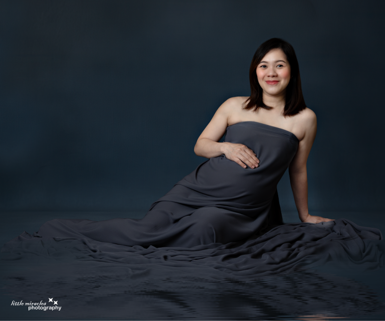 Mum-to-be seated in dark draped fabric on a deep blue backdrop