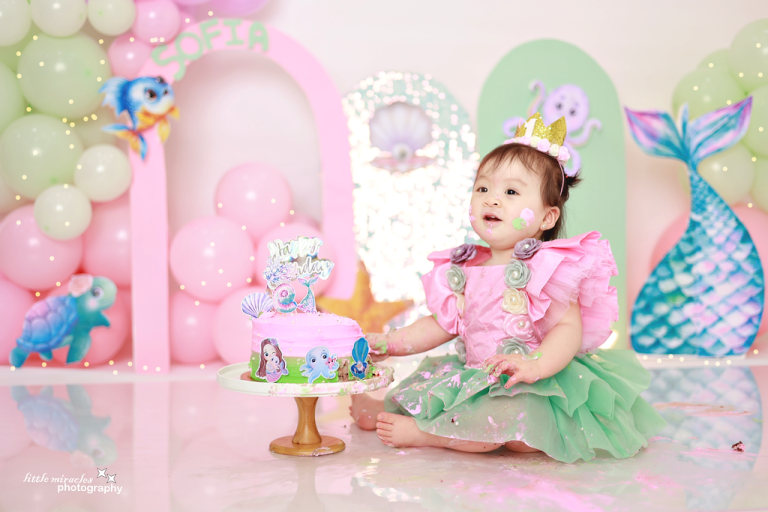Baby girl in a crown at a mermaid-themed cake smash setup
